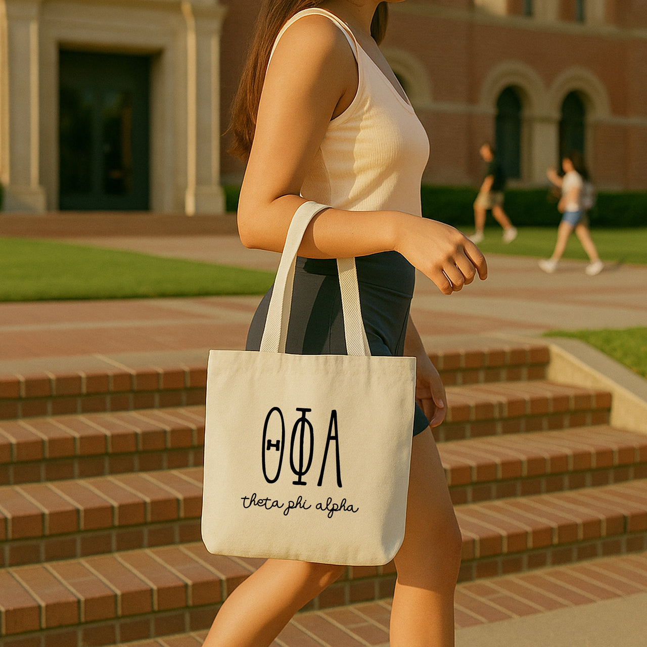 College student carrying a Theta Phi Alpha small canvas tote bag with striped Greek letters