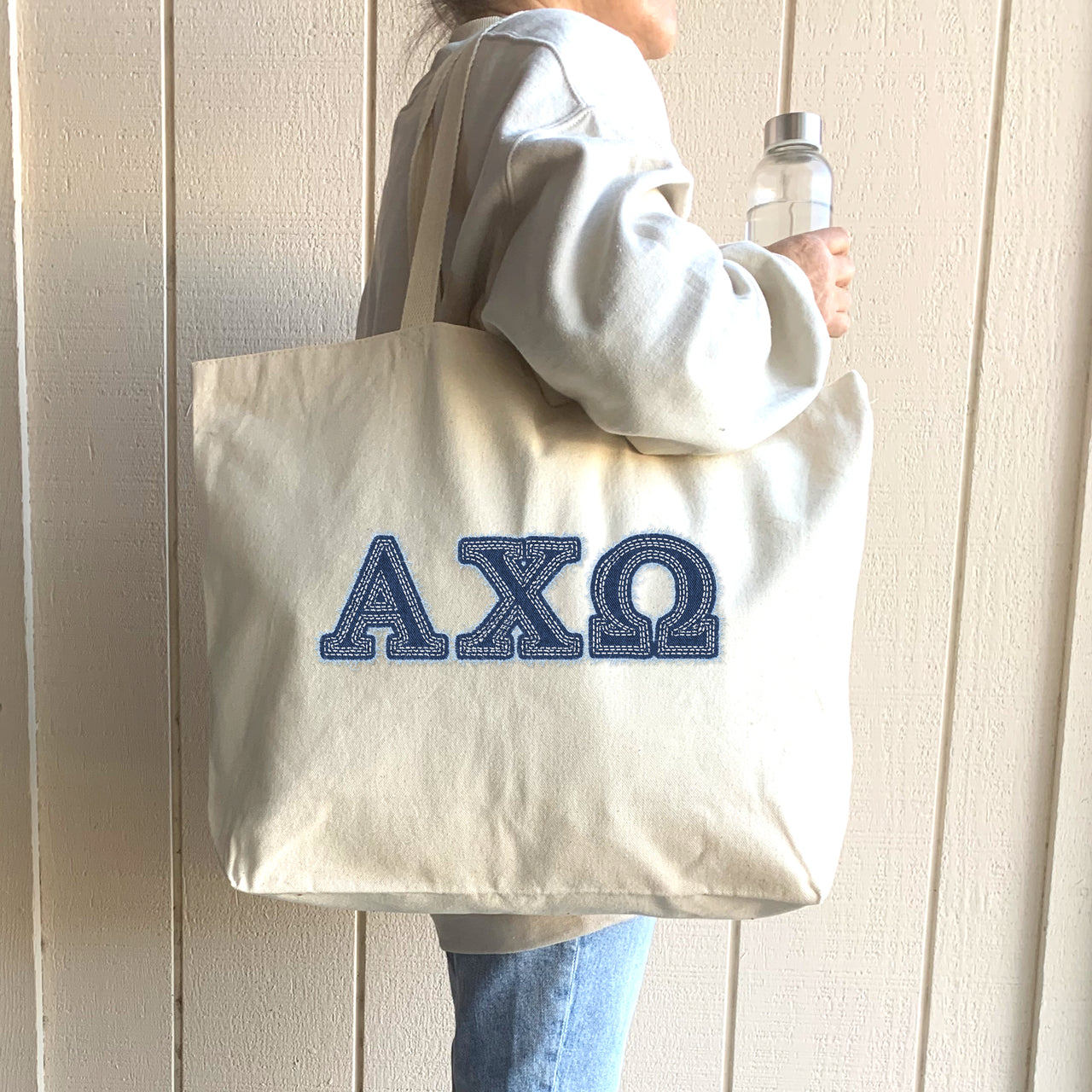 College woman carries a denim Alpha Chi Omega tote over her shoulder on campus