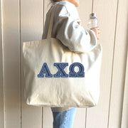 College woman carries a denim Alpha Chi Omega tote over her shoulder on campus