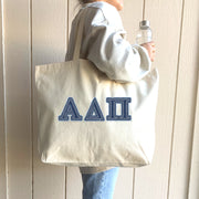 A smiling student carries her canvas tote with denim Alpha Delta Pi letters as she heads to a study session.