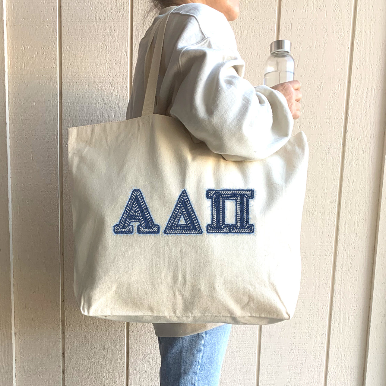 Young woman poses with a denim Alpha Delta Pi tote at a sorority house entrance.