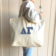 A college woman takes a selfie with her sorority sisters, holding a denim Delta Gamma tote.