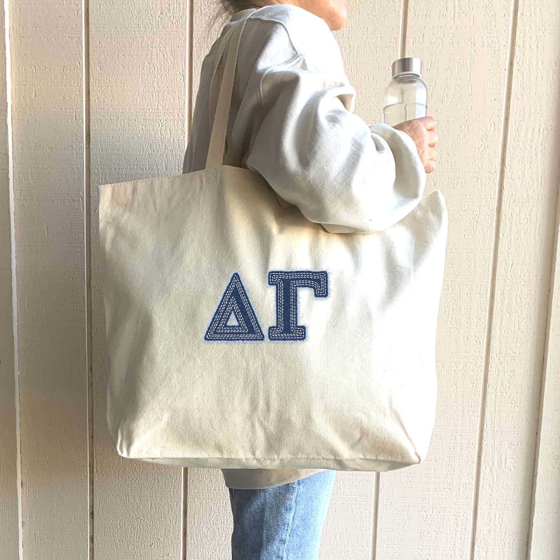 A college woman takes a selfie with her sorority sisters, holding a denim Delta Gamma tote.