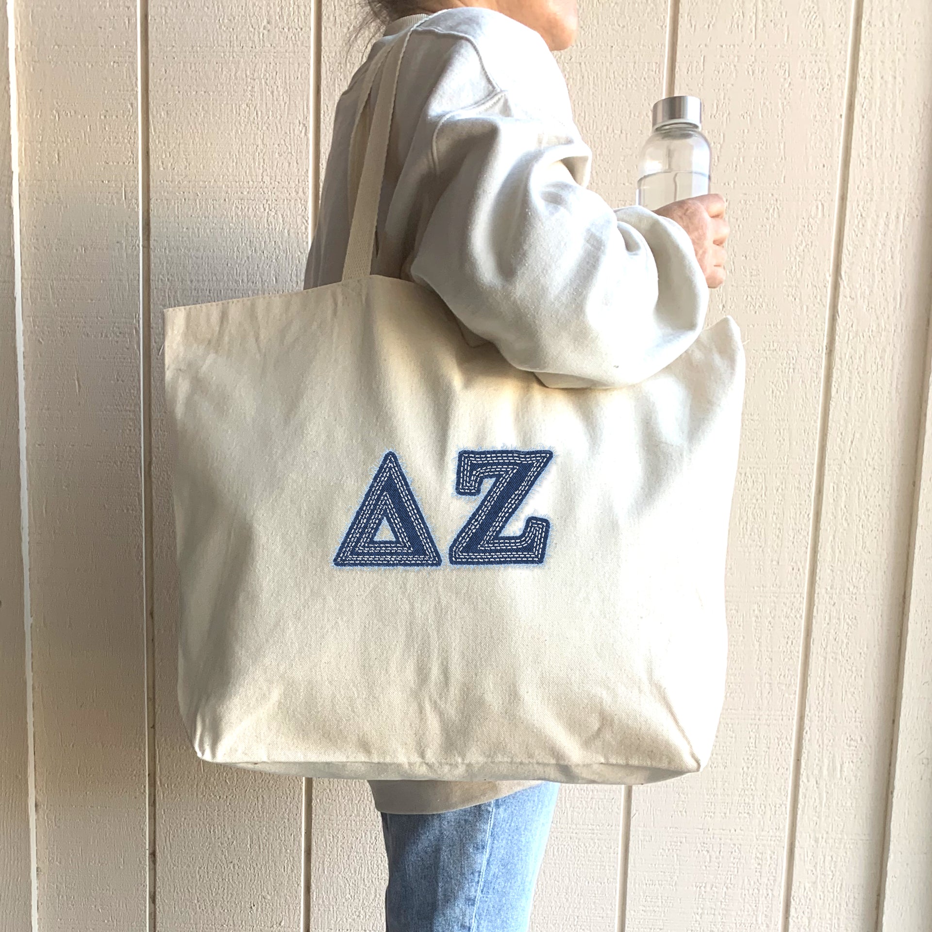 A cheerful woman in a pink hoodie carries a denim Delta Zeta tote while shopping on campus.