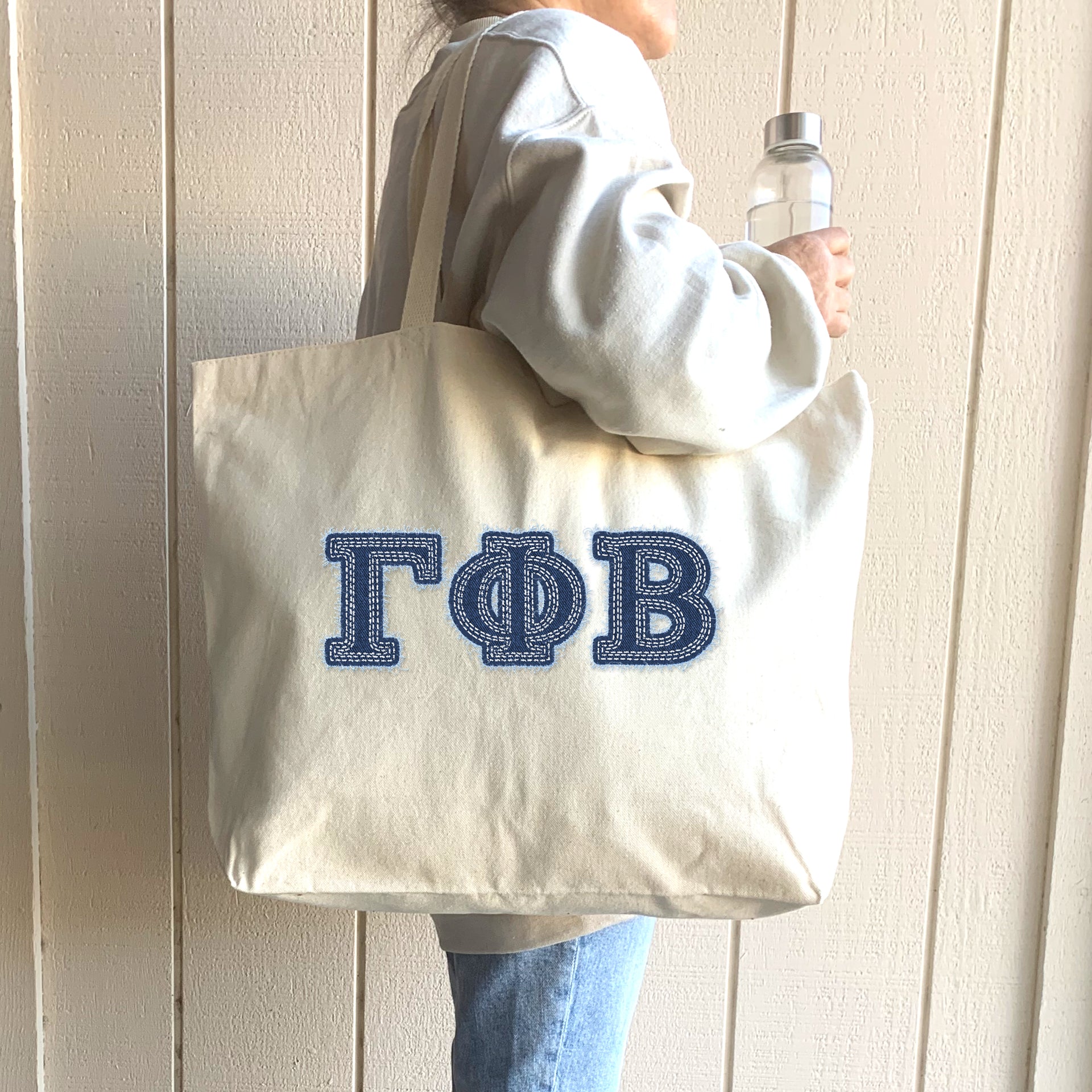 A college woman smiles as she walks to a picnic, her tote with denim Gamma Phi Beta letters swinging by her side.