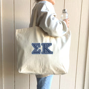 A woman heading to the gym carries a denim-lettered Sigma Kappa tote filled with essentials.