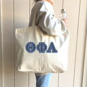 A college woman strolls through the student union with her tote bag showcasing denim Theta Phi Alpha letters.