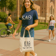 College student carrying a Kappa Alpha Theta small canvas tote bag with striped Greek letters