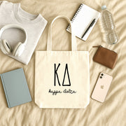 Kappa Delta small canvas tote bag with striped Greek letters styled in a flat lay with everyday essentials