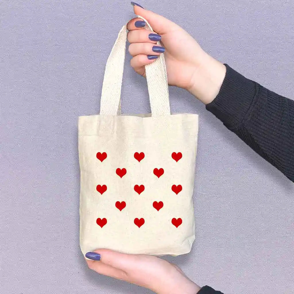 Mini canvas tote bags with all over heart design digitally printed in the color of your choice sold in a pack of four. 
