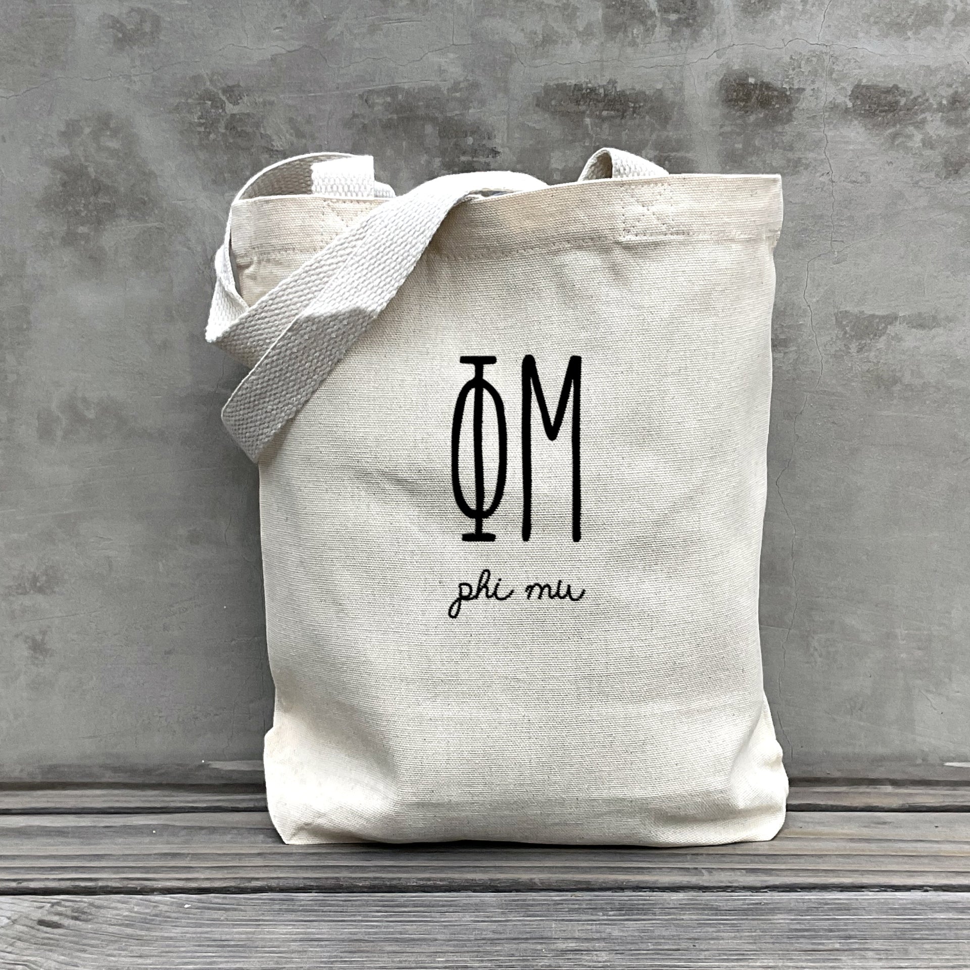 Phi Mu lifestyle image of a Phi Mu tote bag hanging on a dorm door, styled with the sorority’s name in retro font.