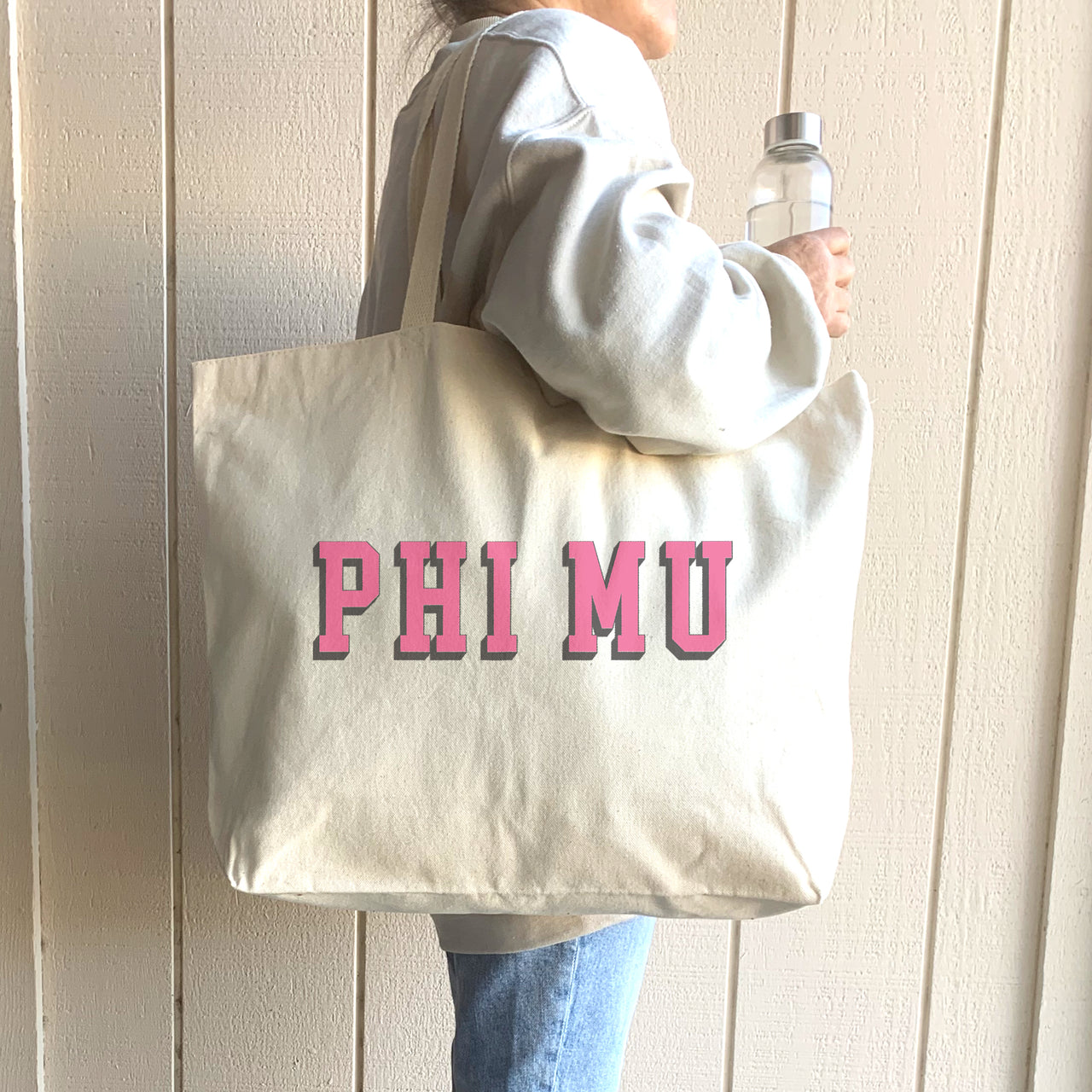 Phi Mu tote with raised lettering, shown worn on the shoulder by a smiling Phi Mu sister in sneakers.