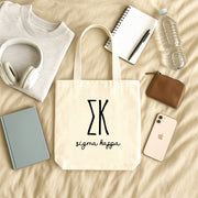 Sigma Kappa small canvas tote bag with striped Greek letters styled in a flat lay with everyday essentials