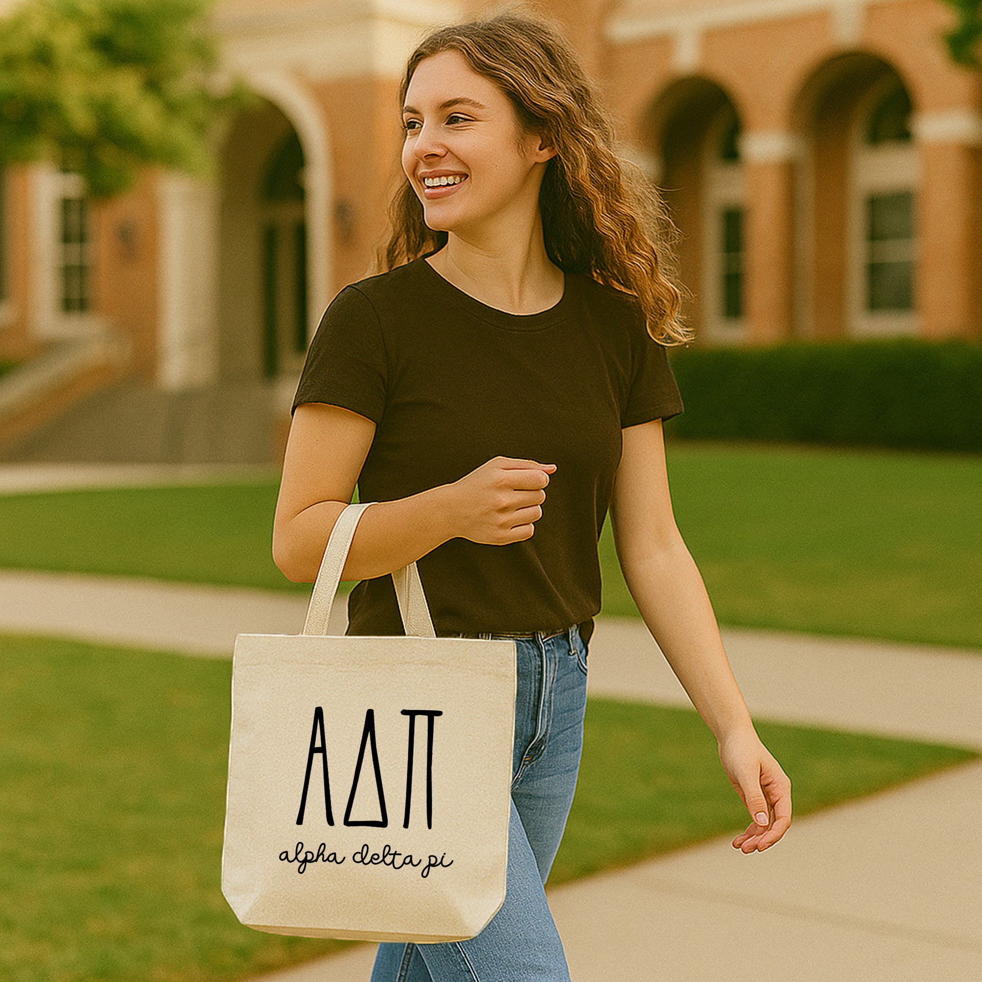Alpha Delta Pi tote bag resting on a bench next to a student, featuring the sorority’s Greek letters in a dimensional font.