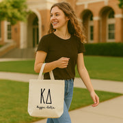 Kappa Delta woman walking into a sorority house holding her small tote bag with bold KD Greek letters.