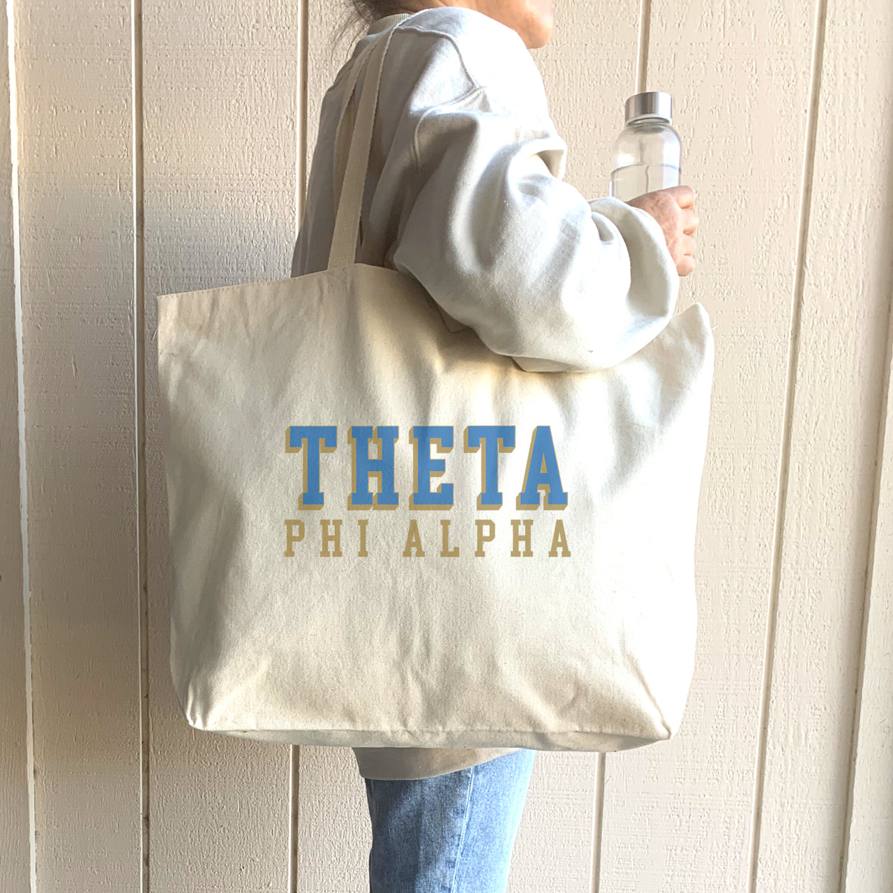 Theta Phi Alpha sorority tote with bold raised text, slung over the shoulder by a member smiling for the camera.