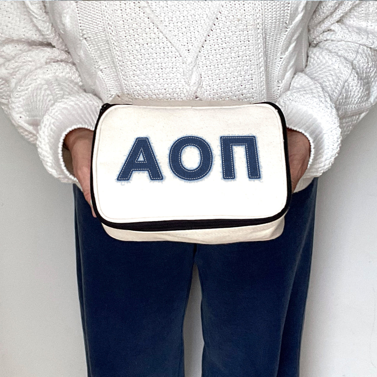Alpha Omicron Pi canvas makeup bag with AOII Greek letters in a denim-style print, held in hand.