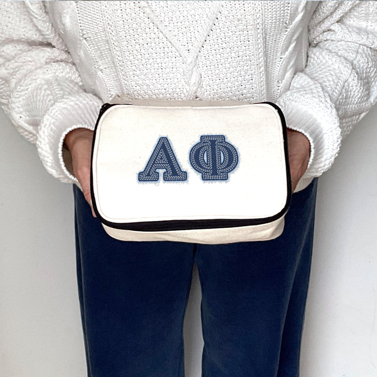 Alpha Phi sorority member holding a cosmetic pouch printed with Alpha Phi denim-style Greek letters.