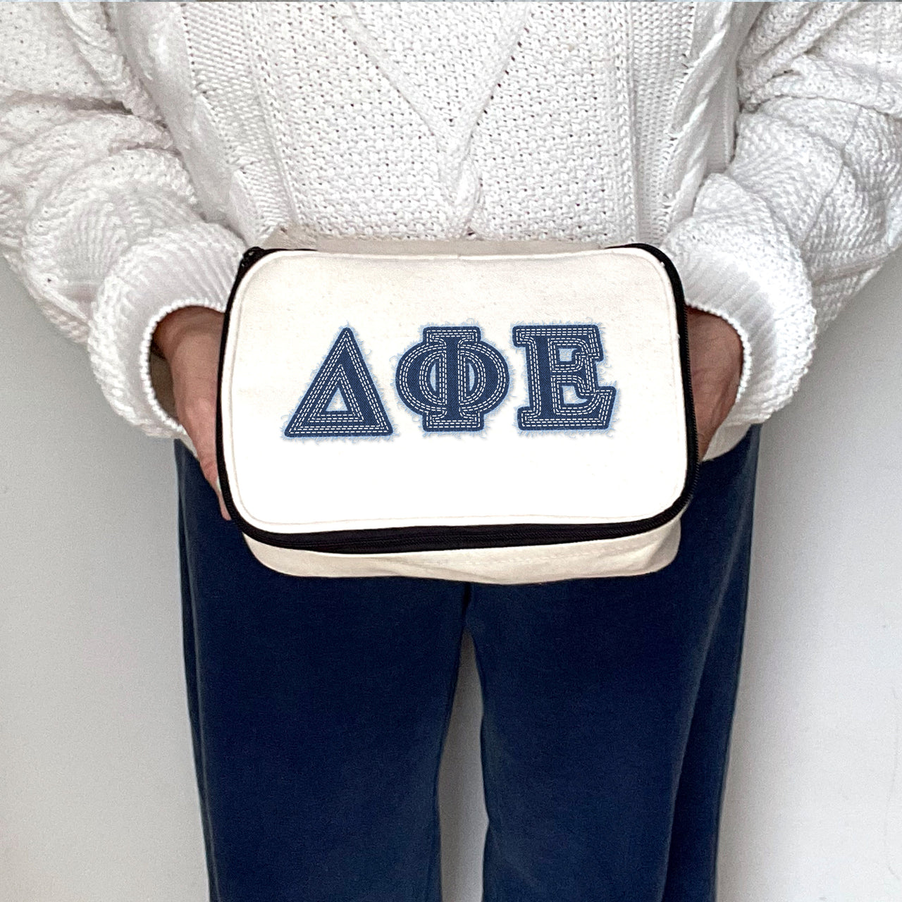 Delta Phi Epsilon cosmetic pouch with DPhiE letters in denim print, shown held by a sorority woman.