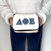 Delta Phi Epsilon cosmetic pouch with DPhiE letters in denim print, shown held by a sorority woman.