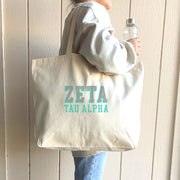 Zeta Tau Alpha tote bag with dimensional sorority letters, carried over the shoulder of a woman in ZTA gear.
