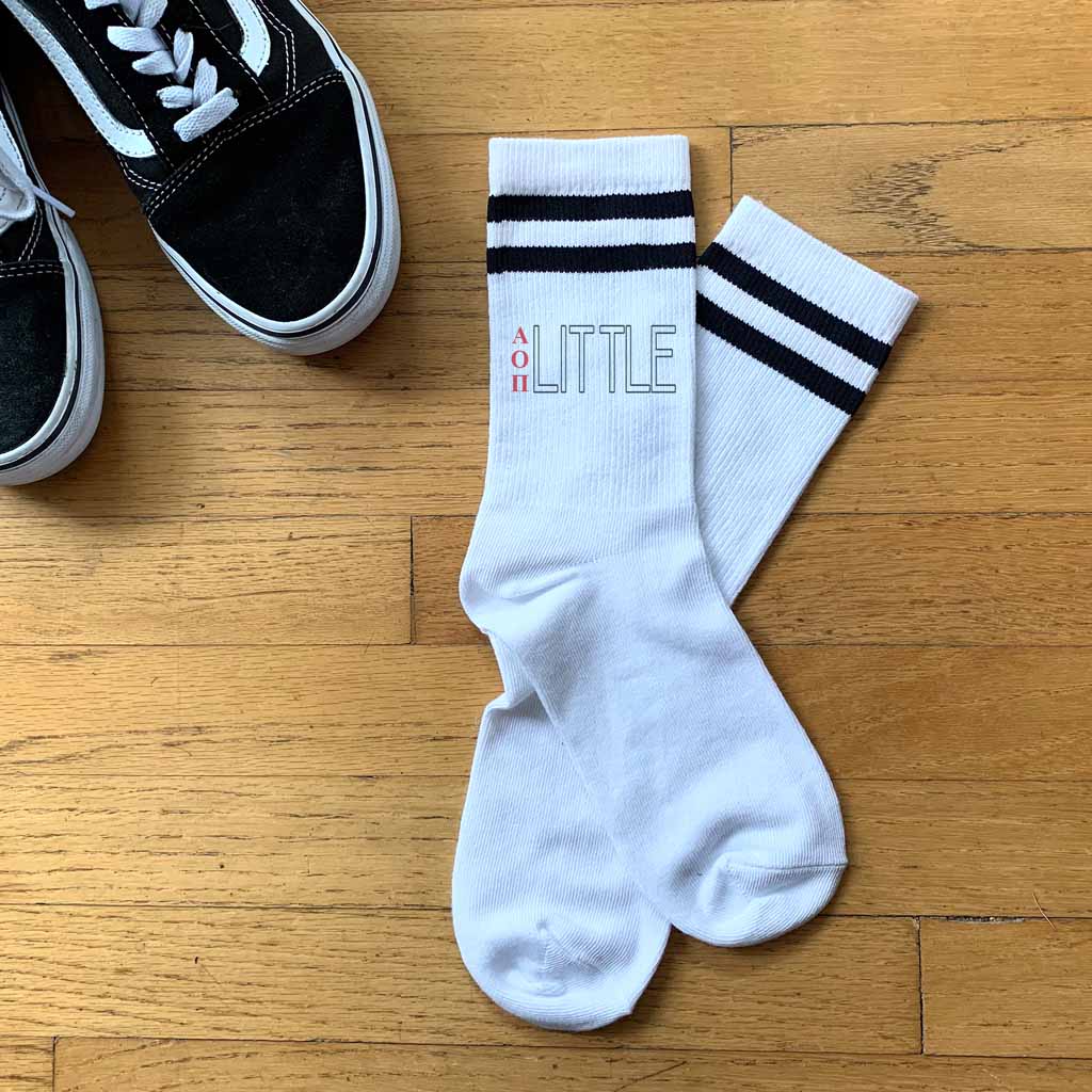 AOP Greek letters printed vertically with a big or little design digitally printed on the outside of both striped cotton crew socks.