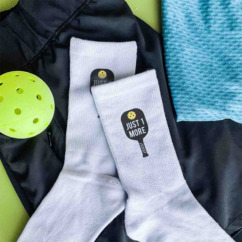 Cute pickleball design with paddle and ball with just one more digitalloy printed on white cotton crew socks.