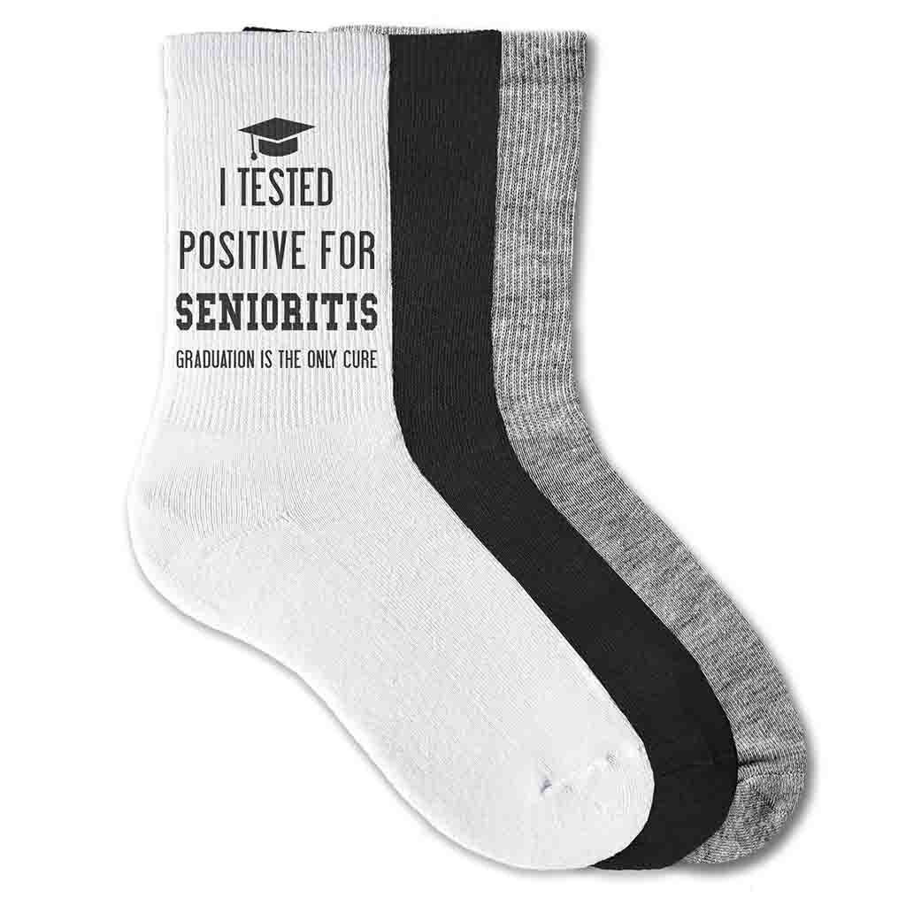 2023 Grad socks for the senior class of 2023 with I tested positive for seniorities graduation is the only cure digitally printed on the side of cotton crew socks.
